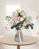 Pink arrangement with 6 roses, mini roses, baby’s breath, and greenery in a glass vase